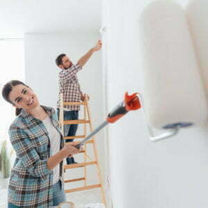 Home makeover and renovation: young happy couple painting their new house interiors using paint rollers