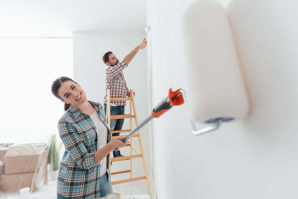 Home makeover and renovation: young happy couple painting their new house interiors using paint rollers
