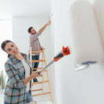 Home makeover and renovation: young happy couple painting their new house interiors using paint rollers